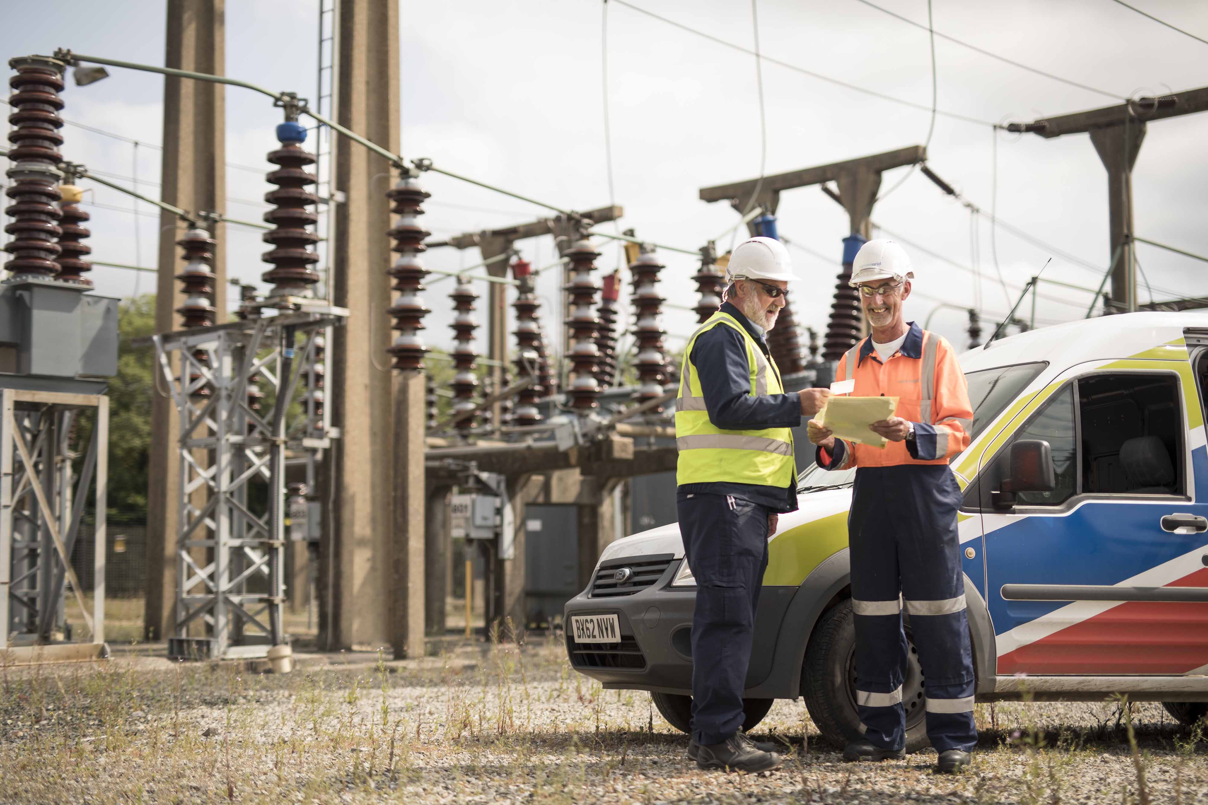 Two National Grid employees standing in front of an electricity plant and a National Grid vehicle 