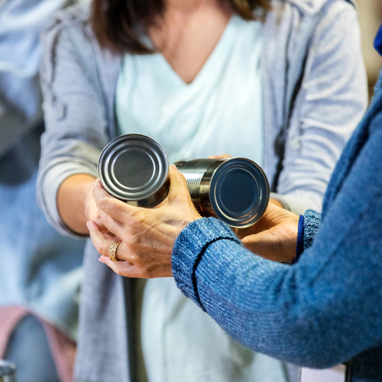 Woman passing two food tins to another person - used for the National Grid story 'Making a difference during the coronavirus outbreak'