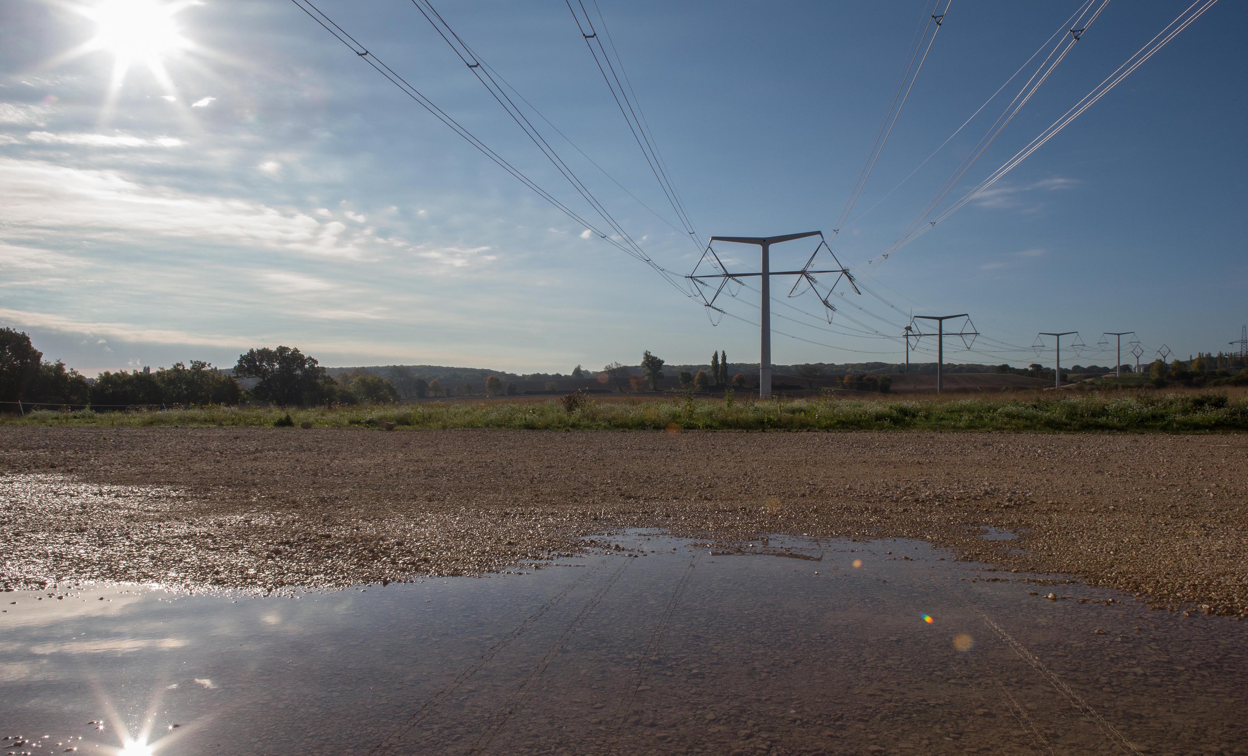 A muddied wet patch of land with grass and electricity structures stretching into the background 