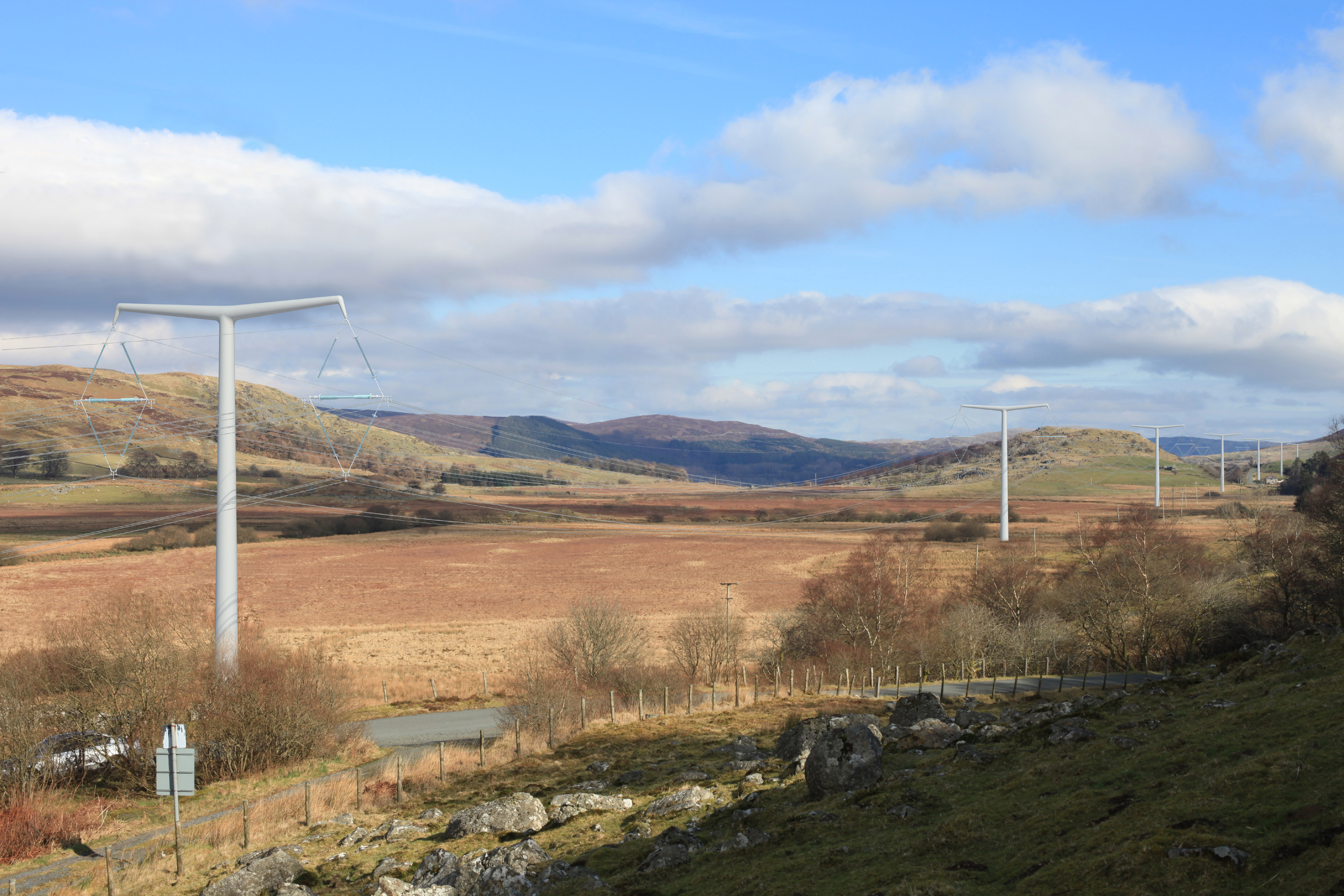 An overview of Lake Bala under a cloudy blue sky with electricity masts extending into the background 
