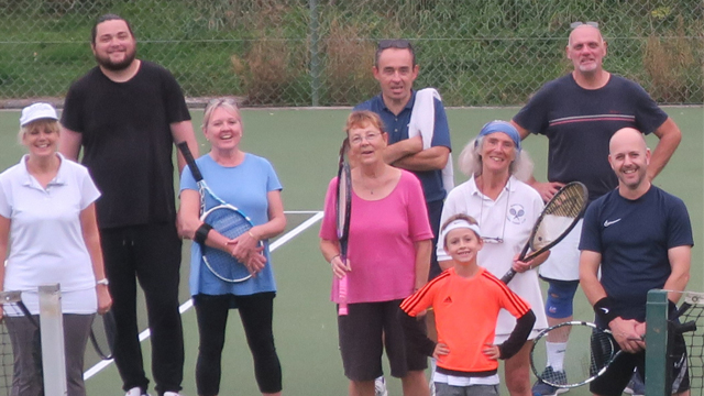 Group of people, some holding tennis rackets, on a tennis court