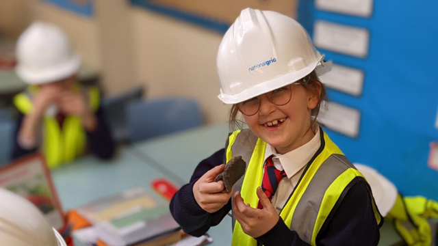 Child wearing National Grid hardhat and hi-vis vest in classroom