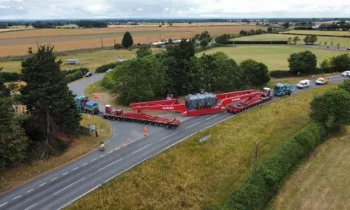 Photograph of the supergrid transformer delivery making its final turn onto Overton Road from the A19. Behind the delivery vehicle there is a convoy of vehicles.  