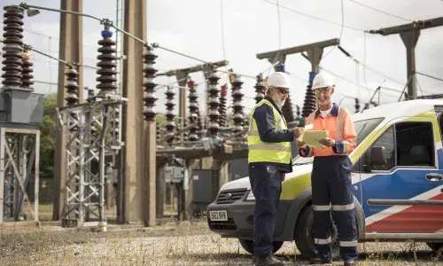 Two National Grid employees standing in front of an electricity plant and a National Grid vehicle 