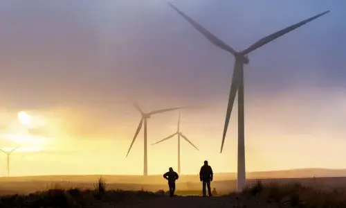 People walking across fields next to wind turbines - used for the National Grid story 'National Grid launches green bond to fund sustainability projects'