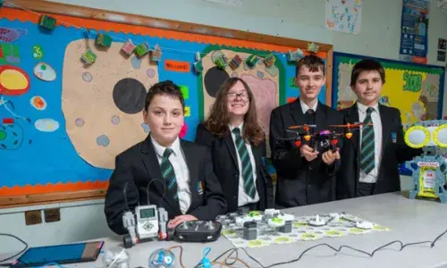 Young students wearing school uniform behind table with STEM equipment, including a drone