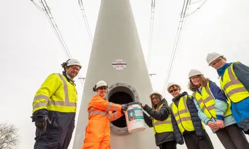 Students wearing hard hats and high-vis vests placing time capsule inside t-pylon