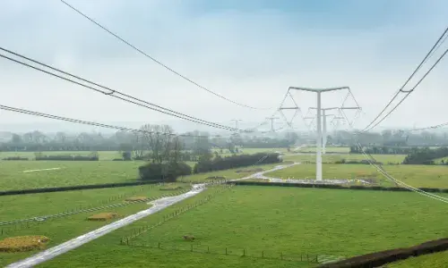 New electricity T-pylons with overhead lines across green fields