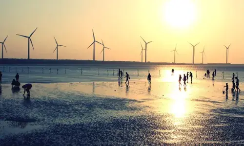Silhouettes of people on a beach at sunset with wind turbines out at sea in the background