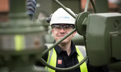 An image of a gas engineer working on-site, wearing a hard hat and a hi-vis vest