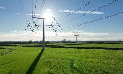 T-pylons and overhead electricity lines in the sunshine in green fields