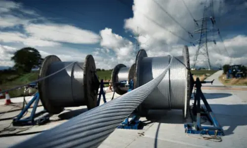 Large spools of overhead electricity lines with electricity pylon in the background