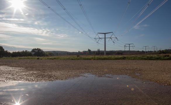 A muddied wet patch of land with grass and electricity structures stretching into the background