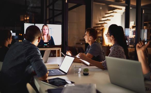 A group of individuals sitting around a table in front of a conference call screen