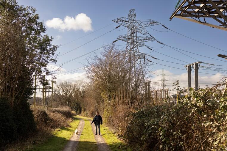 Person walking a dog on a countryside path by an electricity substation and pylons