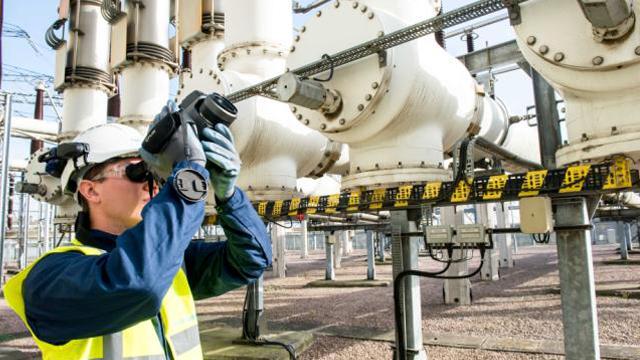 EnergyExplained_SF6LeakDetection_BarkingSubstation_640x360.jpg Man wearing PPE using camera to detect SF6 leaks at substation