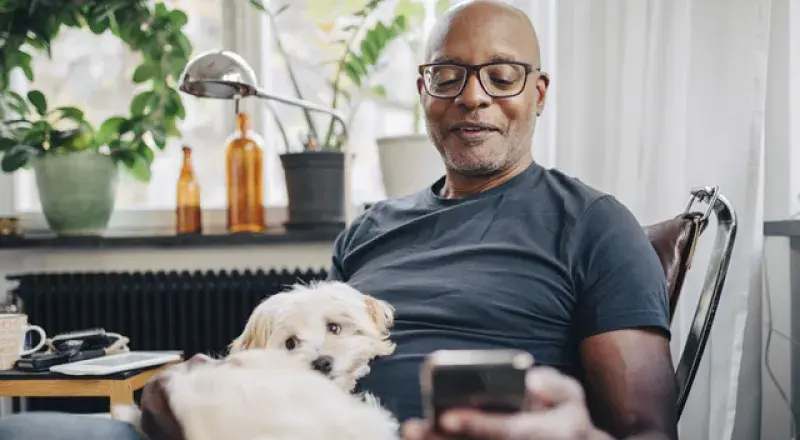 Man looking at a smartphone with a dog on his lap